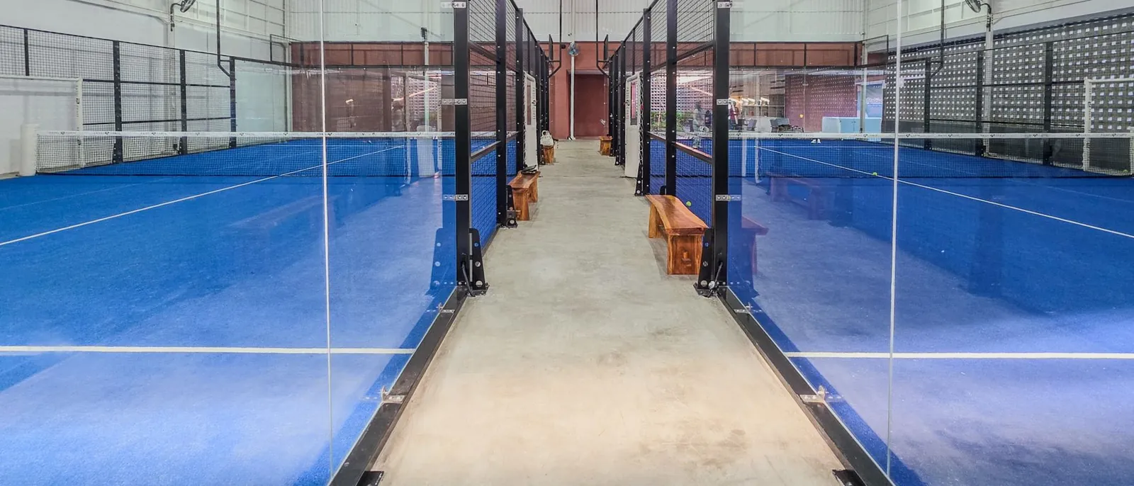 Binnenbanen voor padel met glazen wanden en blauwe vloer